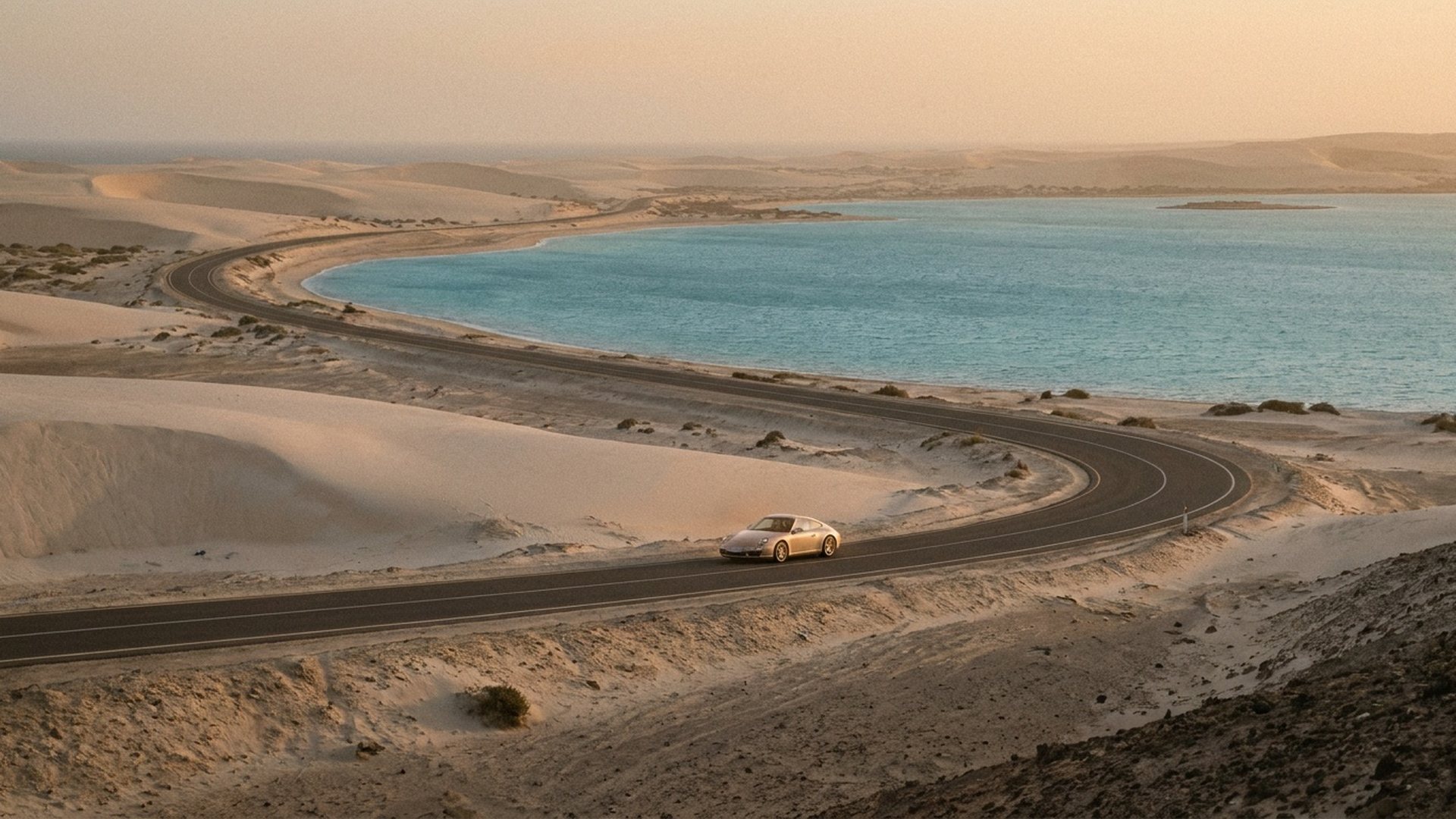 Route sinueuse qui longe une côte au soleil du soir, une voiture claire sans marque dans le virage